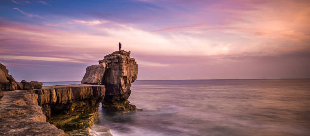 Man standing on top of Pulpit Rock at sunset, Portland Bill on the Isle of Portland near Weymouth on Dorset's Jurassic Coast. England. UK.