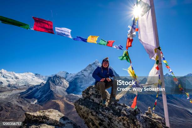 Asian Hiker Sitting On The Cliff In Nangkartsang Peak Everest Base Camp With Himalayan Mountain Range At The Background Stock Photo - Download Image Now