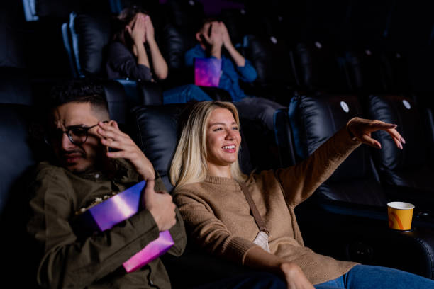 istock Young smiling woman pointing at large screen while watching action movie 1200360802