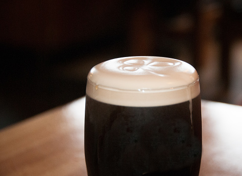 Close-up photo of a glass of dark beer with foam and shamrock