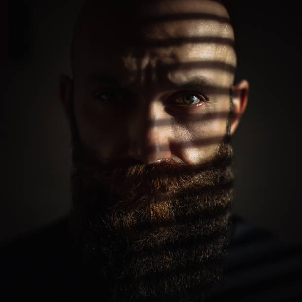 istock Close-up portrait of middle aged brutal bearded man with expressive eyes and striped shadows on his face 1200377708