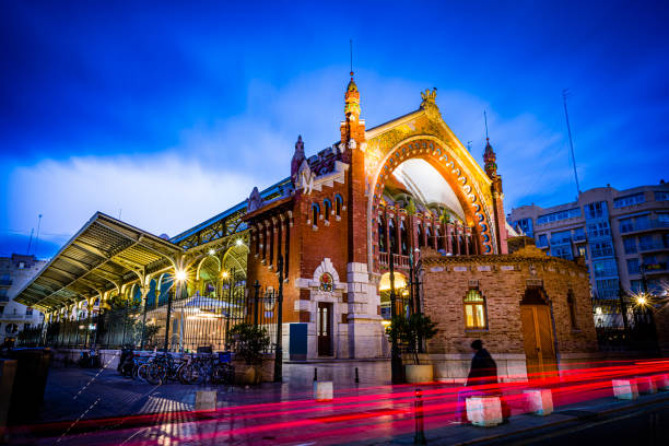 Valencia, Spain. Monday,  18th of November 2024. The photo captures a vibrant scene inside the iconic Central Market of Valencia, Spain. Known locally as Mercado Central, this historic market is one of Europe’s oldest functioning food markets and a landmark of modernist architecture. The interior features a stunning combination of historical charm and contemporary functionality, with colorful stalls offering fresh produce, meat, fish, and regional delicacies. Natural light streams through the market's glass windows, highlighting the intricate ironwork and decorative ceramic tiles. This image perfectly encapsulates the dynamic atmosphere of this cultural hub, making it ideal for travel publications, culinary blogs, or architectural features.