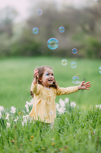 Sweet little girl catching bubbles in the field