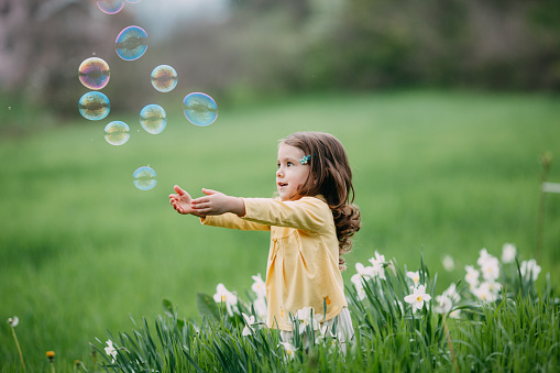Sweet little girl catching bubbles in the field
