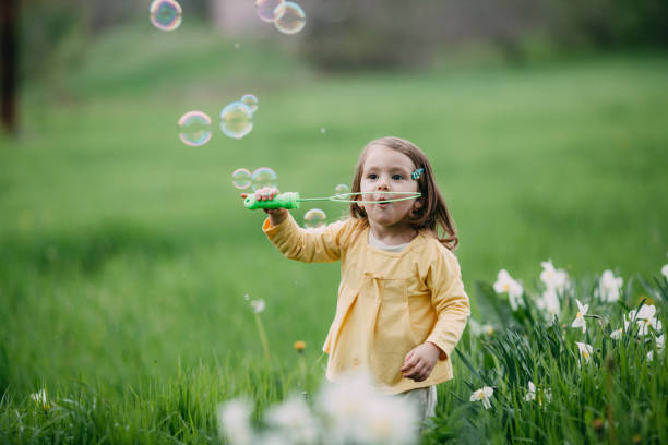 Sweet little girl catching bubbles in the field