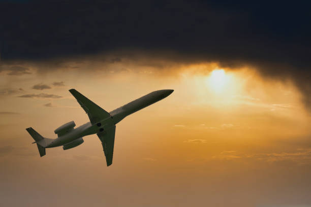 istock Airplane flying high in dark storm clouds and bright sun during sunset 1200384252
