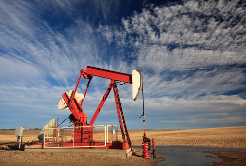 A red oil pumpjack on the prairie with dramatic sky. Image taken in Southern Alberta, Canada. Nobody is in the image. Location is two hours southeast of Calgary.