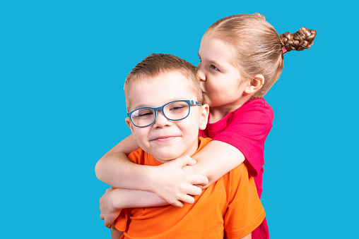 Brother and sister hugging and smiling. Isolated on a blue background. For any purpose.