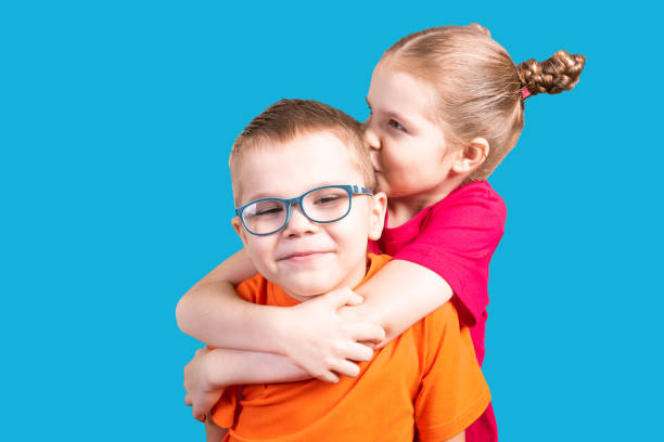 Brother and sister hugging and smiling. Isolated on a blue background. stock photo
