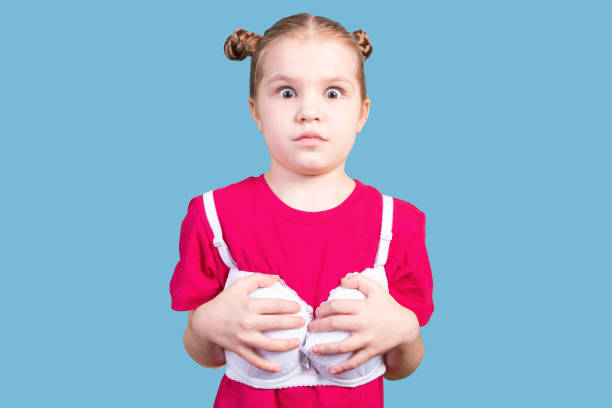 Little girl in mom's bra, with a funny expression on her face. Isolated on a pink background. stock photo