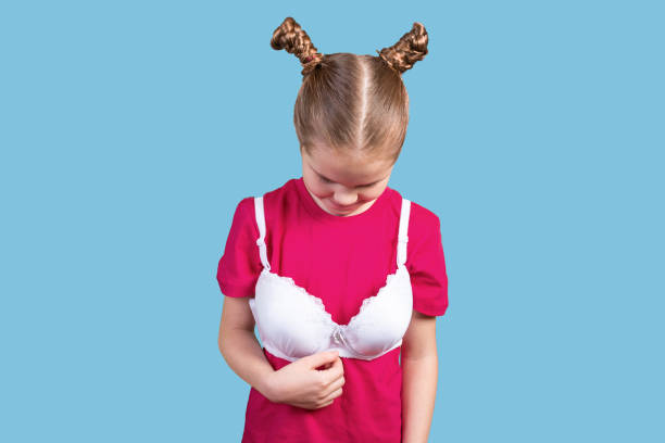 Little girl in mom's bra looking down. Isolated on a blue background. stock photo