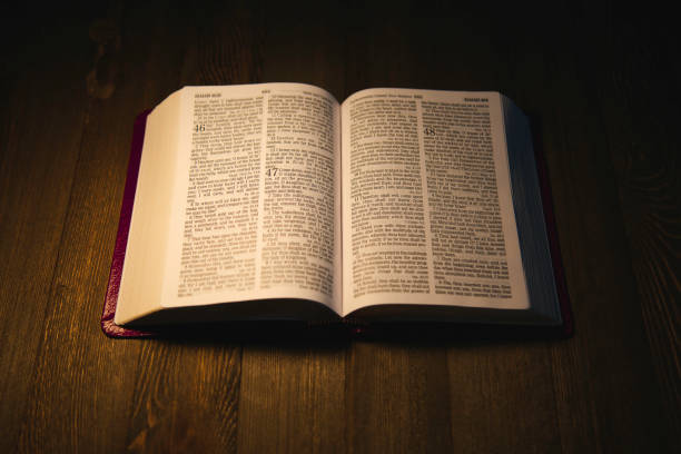 istock Open Holy Bible over a wooden table at night 1200400397