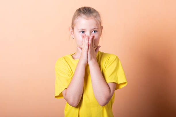 istock Beautiful little girl is embarrassed on a light orange background. 1200402421