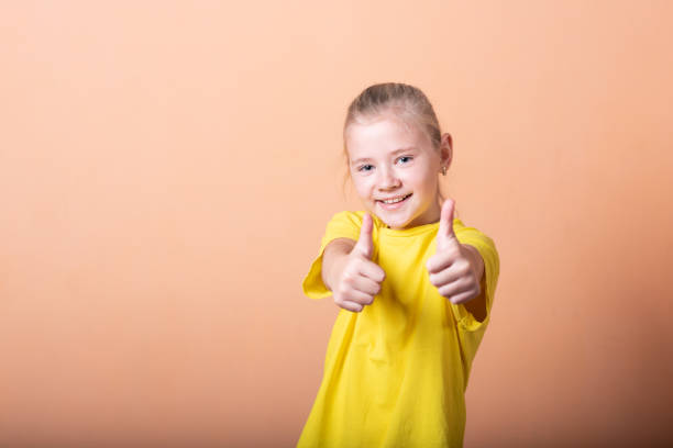 istock Girl showing thumbs up, on a light orange background. 1200402463