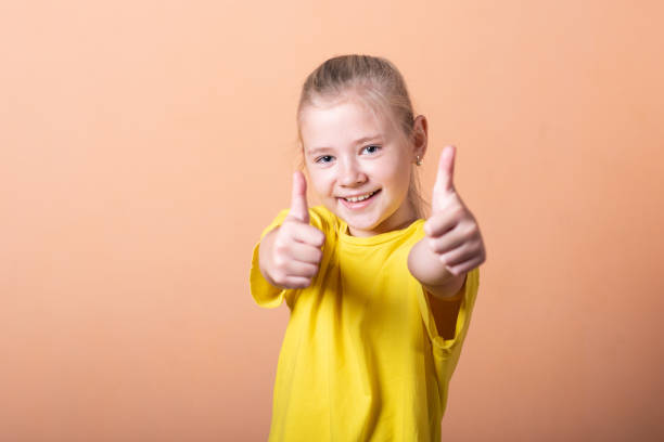 istock Girl showing thumbs up, on a light orange background. 1200402478