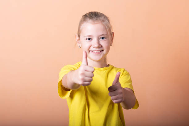 istock Girl showing thumbs up, on a light orange background. 1200402495