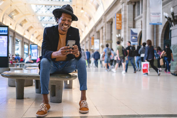 istock Cheerful man text messaging on a mobile phone on a train station 1200408542