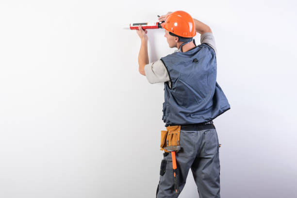 Builder with sealant. In work clothes and hard hat. On a light gray background. stock photo