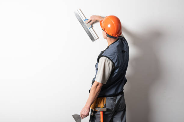 istock The builder smoothes the wall with a spatula. In work clothes and hard hat. On a light gray background. 1200410199