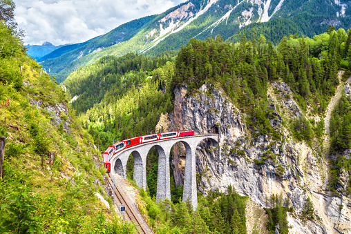 Landwasser Viaduct in summer, Filisur, Switzerland. It is landmark of Swiss Alps. Nice Alpine landscape. Red train of Bernina Express on railroad bridge in mountains. Panoramic view of famous railway.