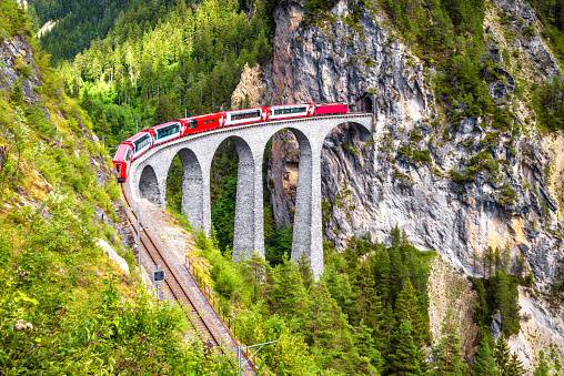 Landwasser Viaduct in summer, Filisur, Switzerland. It is landmark of Swiss Alps. Nice Alpine landscape. Red train of Bernina Express on railroad bridge in mountains. Scenic view of famous railway.