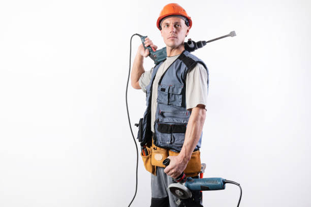 A builder with a hammer drill on his shoulder, and a angle grinder in his other hand, in a helmet, smiles. stock photo