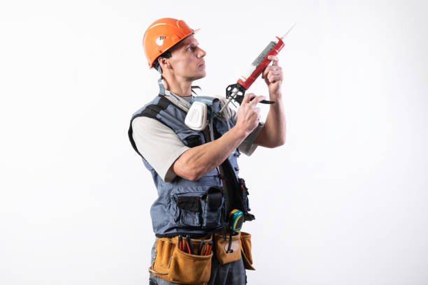 A builder in a helmet, with silicone in a mounting gun. Holds in hands. On a light background. stock photo
