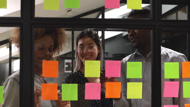 Happy mixed race young colleagues working together near kanban board.