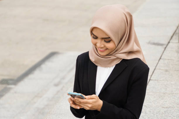 Beautiful asian muslim woman multitasking with her mobile device stock photo