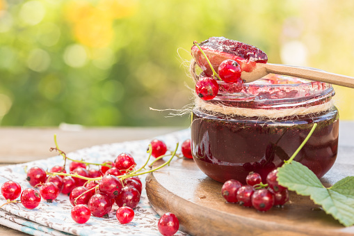 red currant jam and red currant with leaves on a wooden background.