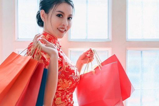 Happy asian chinese woman wearing a qipao dress traditional with shopping bags enjoying in shopping in Chinese new year day.