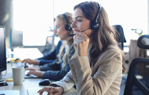 istock Female customer support operator with headset and smiling, with collegues at background. 1200450726