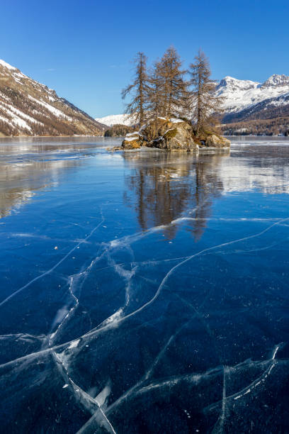 istock Frozen lake with ice cracks on surface with an islet at the background 1200454994