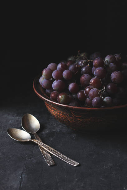 A cluster of an Organic fresh seedless red grapes in a transparent bowl isolated on a white background, selective focus of red grapes in a plate