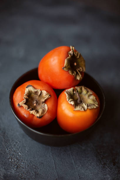 istock Fresh persimmons in black bowl on dark concrete table. 1200470444