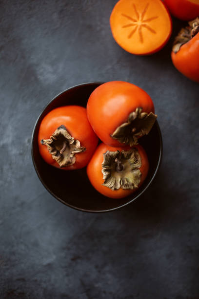 istock Fresh persimmons in black bowl on dark concrete table. 1200470473