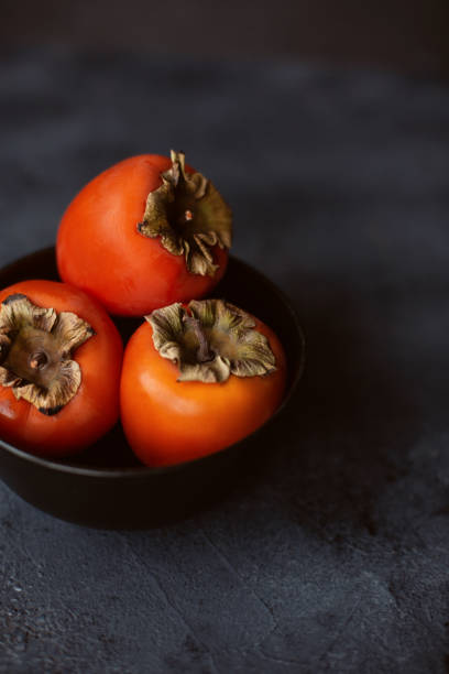 istock Fresh persimmons in black bowl on dark concrete table. 1200470506