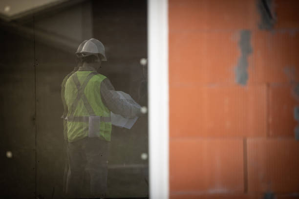 Manual worker showing something to his colleague through a window frame at construction site.