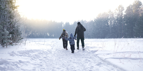 happy family: mother, father and two kid running on the snowy country road in wintertime at sunset