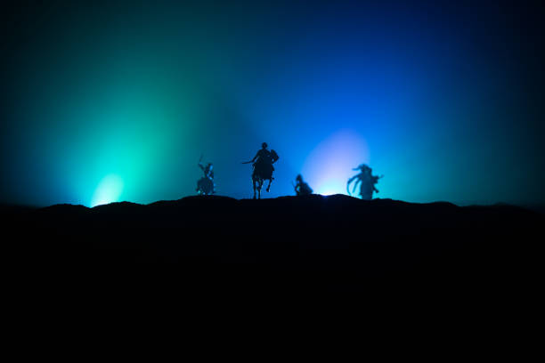 istock Medieval battle scene with cavalry and infantry. Silhouettes of figures as separate objects, fight between warriors on dark toned foggy background. Night scene. 1200475057