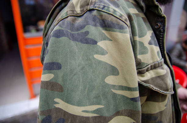 A man in a 3D leaf style light weight Ghillie suit and face paint camouflage with an AR-15 rifle with ACOG scope in the woods.