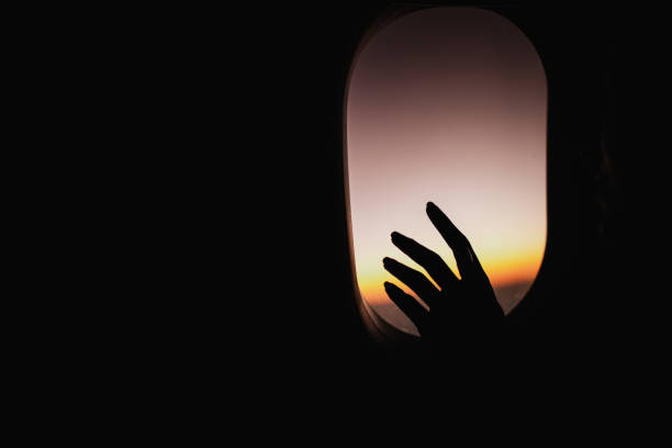 istock Silhouette of a woman's hand on an airplane window at sunset. 1200477007