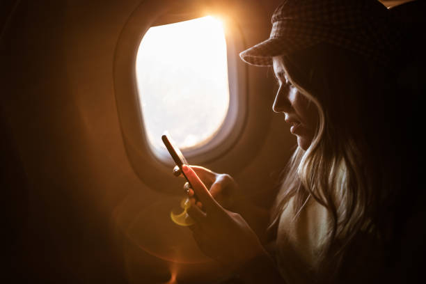 istock Young woman using mobile phone while traveling by airplane at sunset. 1200478482