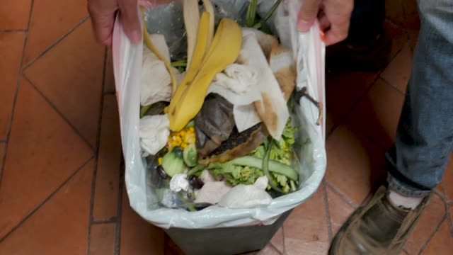Man removes a plastic bag of trash from a kitchen plastic garbage bin