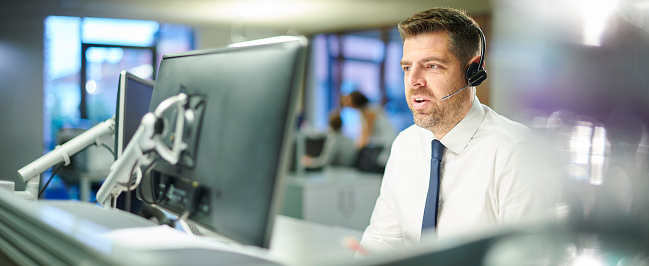 Male analyst in headset watches news, works in bank office on multi-monitor computer with real-time stocks, exchange market charts and commodities. Cryptocurrency trading, investment and analytics.