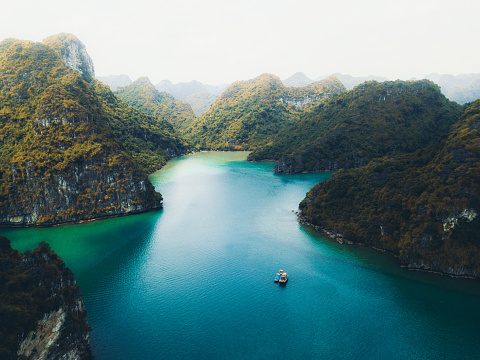 Drone panoramic photo of small islands with rainforest, boat and the sea during bright summer sunrise at Halong Bay, North Vietnam