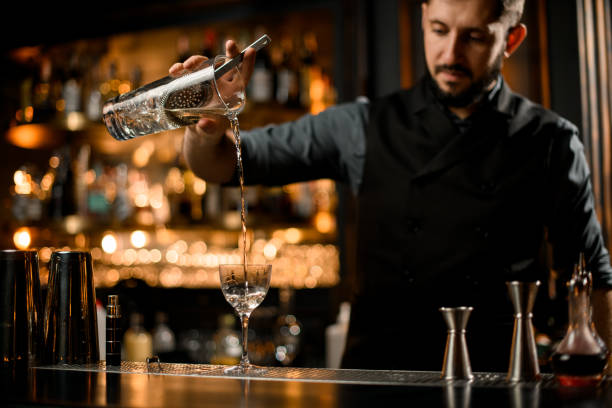 bartender pouring vodka from glass with strainer - men elegance cocktail cool imagens e fotografias de stock