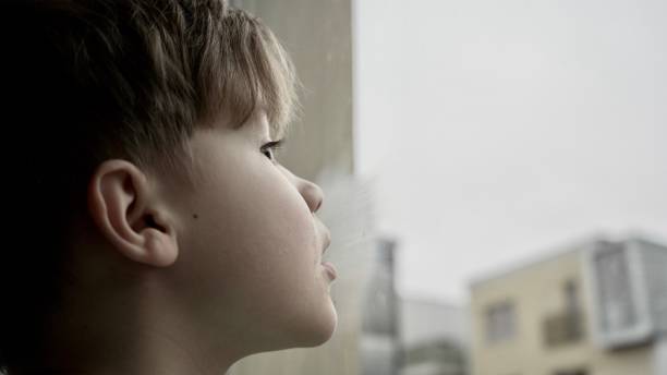 istock Lonely child looking into the window. Bored boy feeling sad on a rainy day. Hopefully looking outside of home. 1200498332