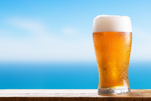cold glass of beer on a wooden table on background of the sea