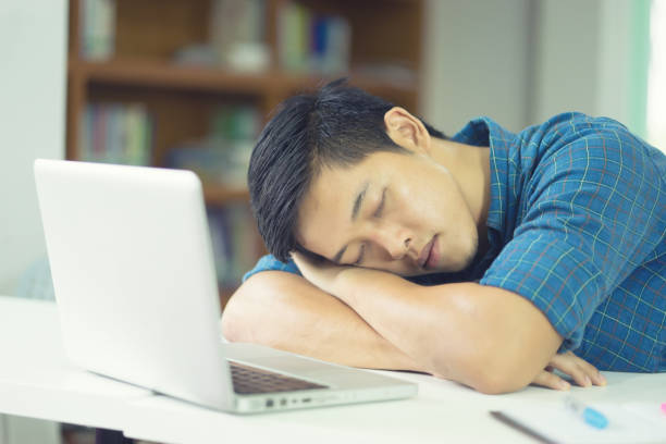 cansado. estudante cansado masculino asiático que dorme em seus livros durante a leitura na sessão cansado dos exames da sala de aula da universidade - sleeping high school desk education - fotografias e filmes do acervo
